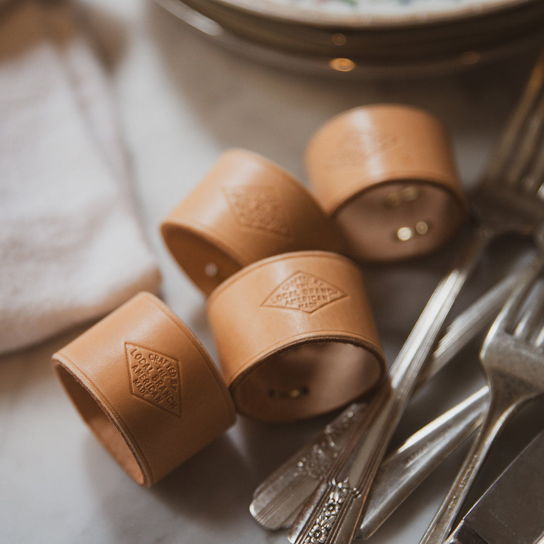 Brown leather cuffs with embossed designs on a white surface with silver cutlery.