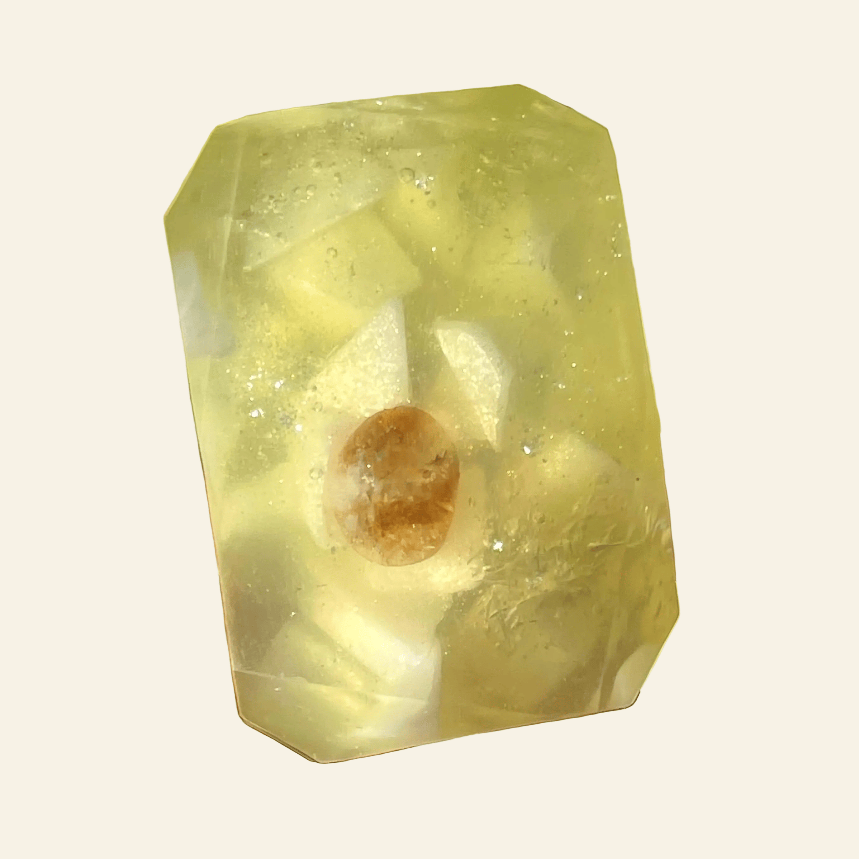 Hand holding a block of yellow soap with a small brown center, against a blurred background of similar soap blocks.