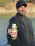 Man holding a bottle of supplements outdoors by a body of water
