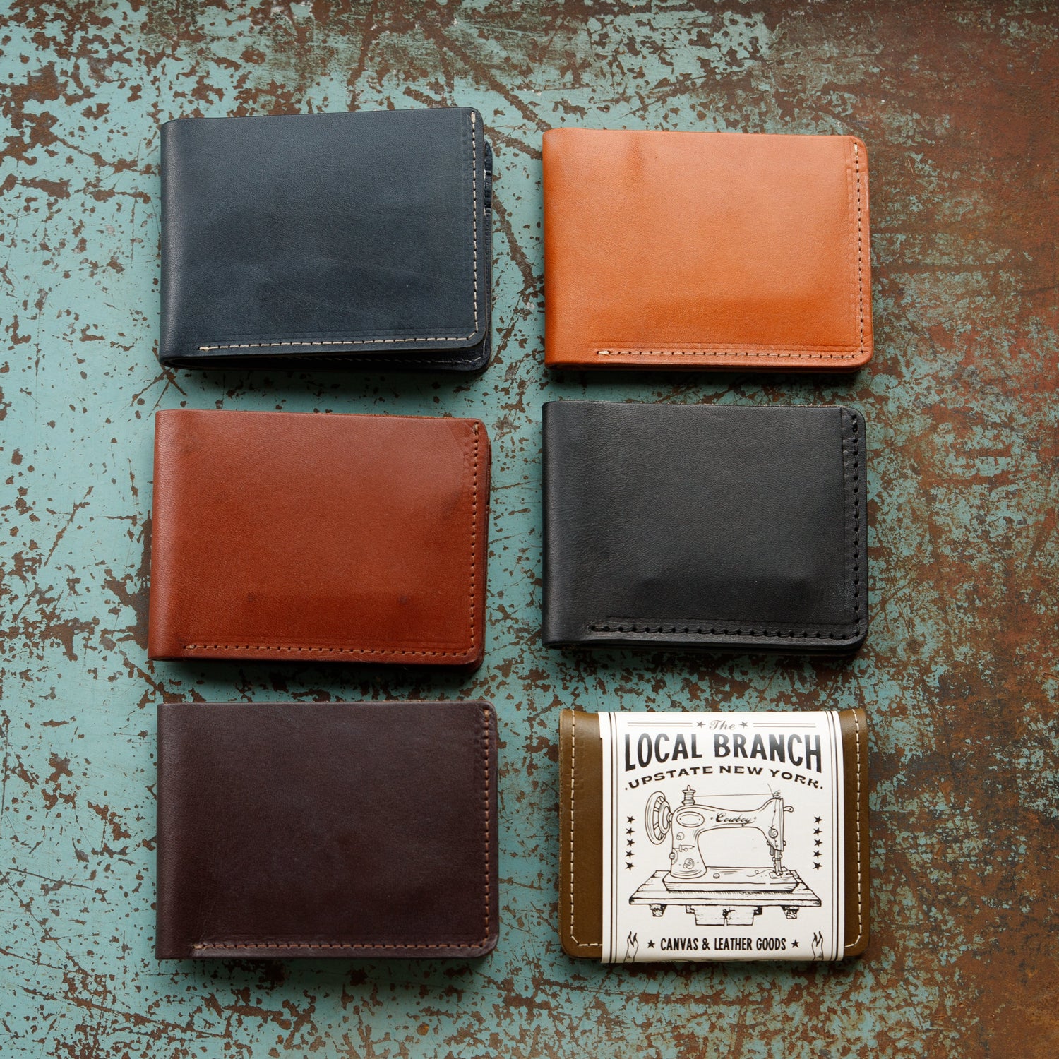 Five leather wallets in different colors on a textured surface with a &