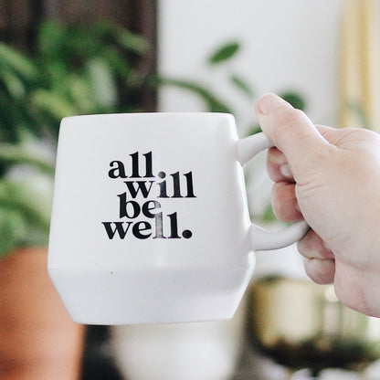 A hand holding a white ceramic mug with the phrase &
