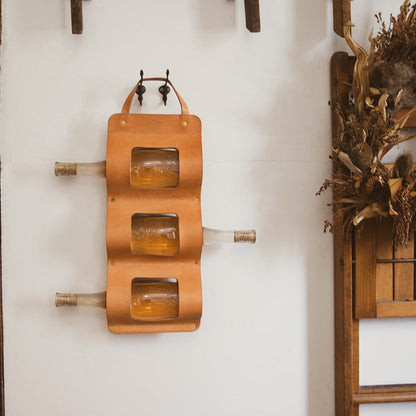 Wall-mounted leather bottle holder with three bottles on a white wall.