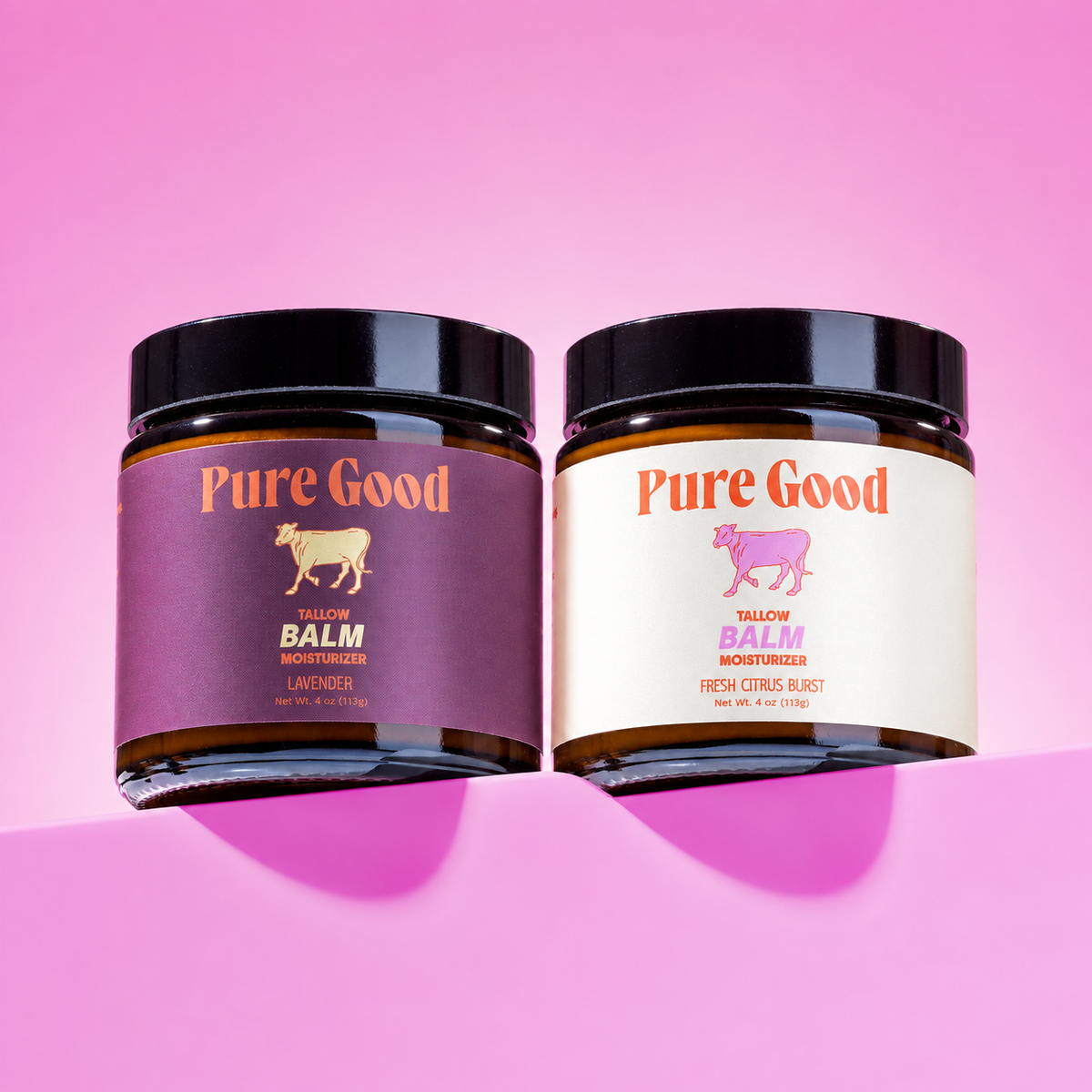 Two jars of Pure Good Tallow Balm on a pink background, one with a purple label and one with a cream label.