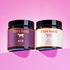 Two jars of Pure Good Tallow Balm on a pink background, one with a purple label and one with a cream label.