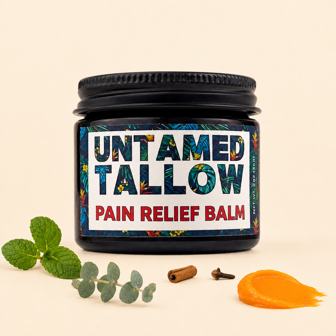A jar of Untamed Tallow Pain Relief Balm with a black lid and a tropical patterned label, styled on a beige background with mint leaves, eucalyptus, cinnamon, cloves, and a smear of orange balm.