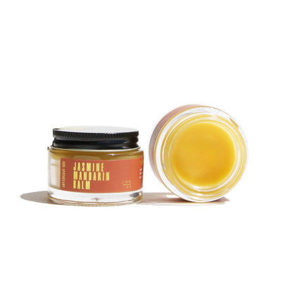 Jar of Jasmine Mandarin balm with a lid off, showing the yellow balm inside on a white background.