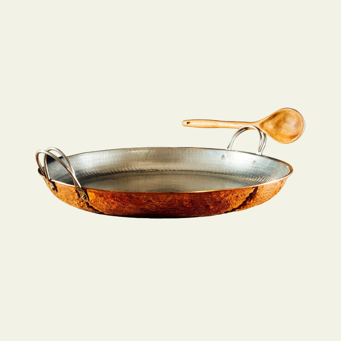 Hammered copper pan with wooden spoon on a rustic wooden surface