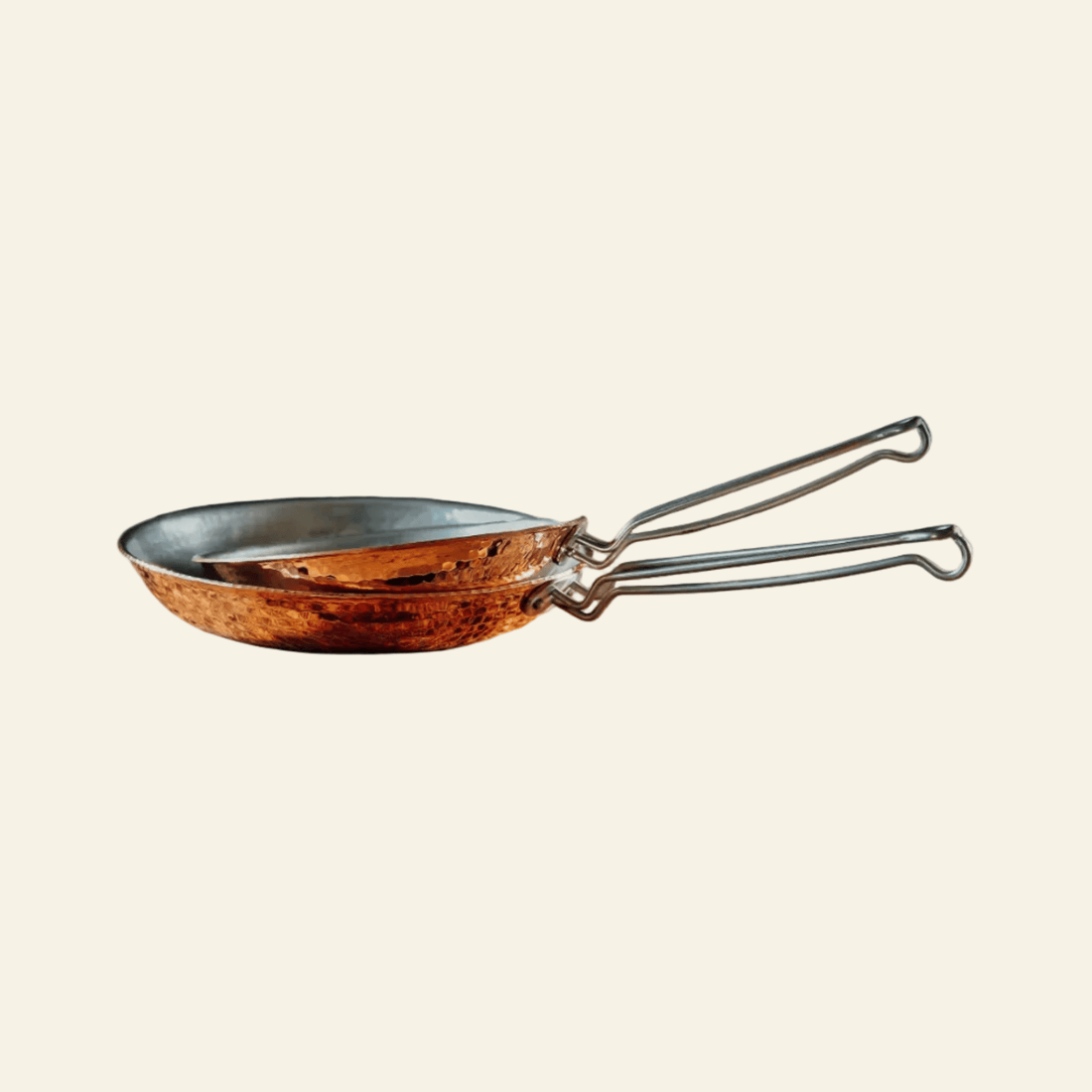 Copper frying pan with metal handles on a light beige background