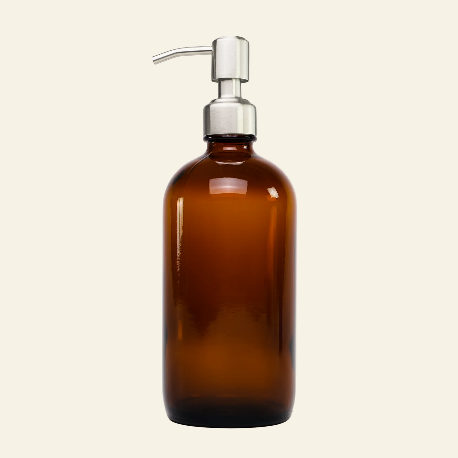 An amber glass bottle with a silver metal pump dispenser, photographed against a seamless light gray studio background.