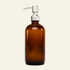 An amber glass bottle with a silver metal pump dispenser, photographed against a seamless light gray studio background.