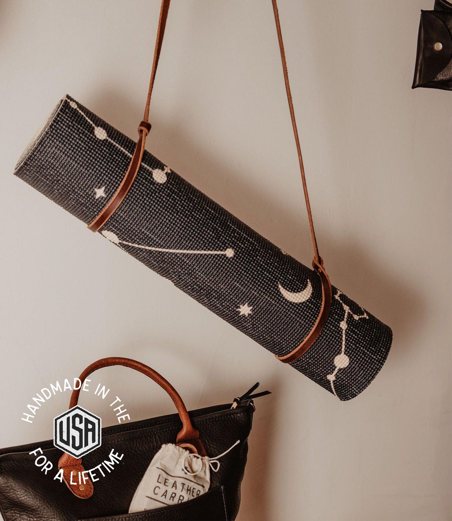 Black yoga mat with star and moon designs on a strap, placed on a white surface.