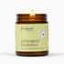 An amber glass jar candle with a lit flame, featuring a pale yellow-green label that reads &