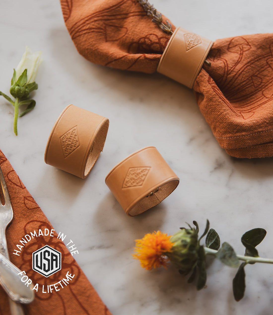 Two brown leather cups with a woven pattern on a marble surface with flowers and a cloth.