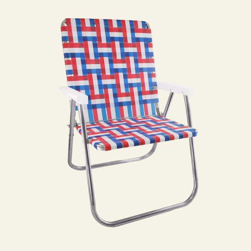 A folding beach chair with a woven red, white, and blue patterned sling seat and backrest, supported by a curved silver metal frame, shown on a plain white background.