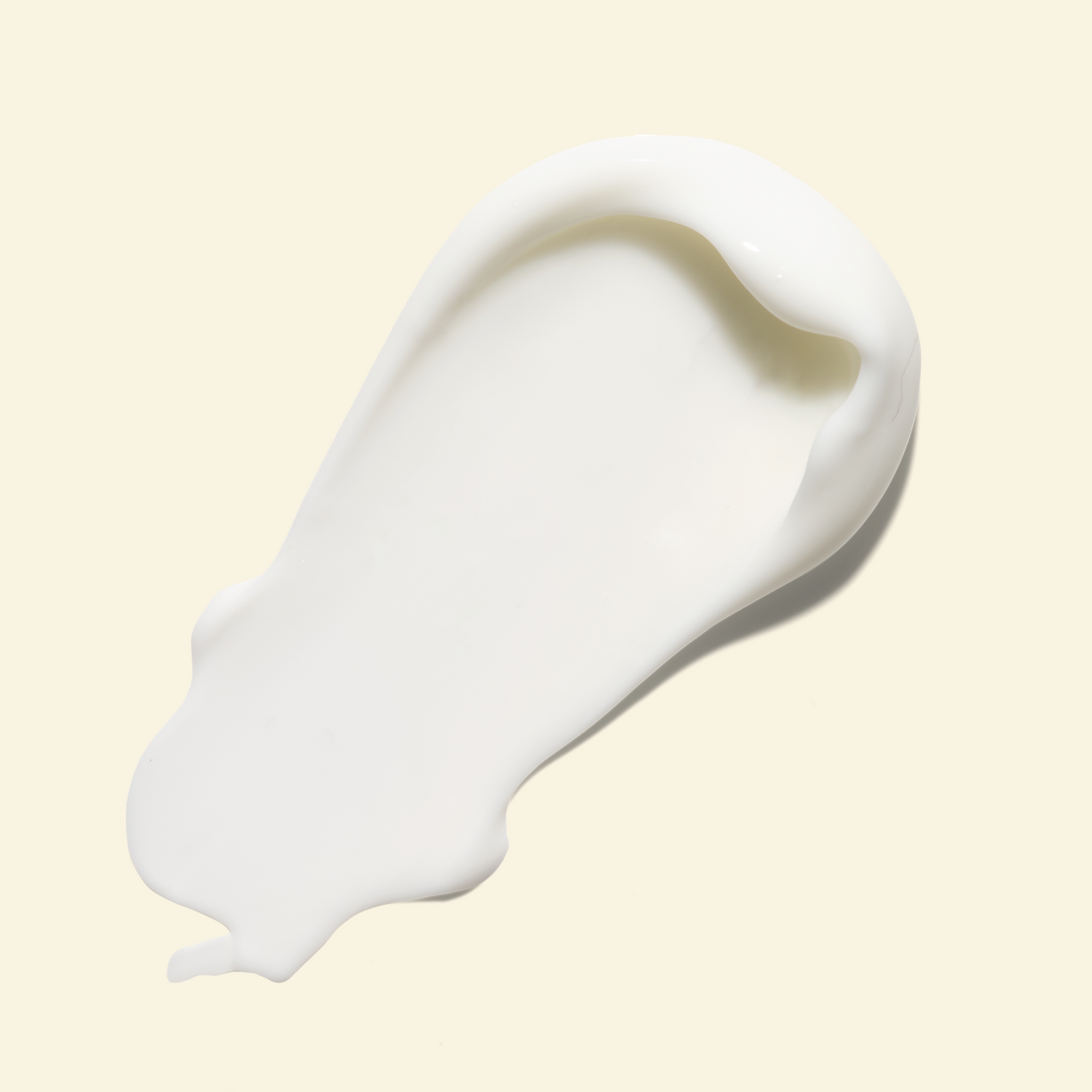 A thick, creamy white product smear, likely a skincare cream or lotion, shown on a solid pale beige background.