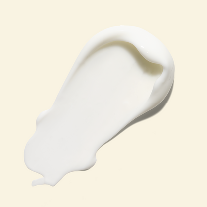 A thick, creamy white product smear, likely a skincare cream or lotion, shown on a solid pale beige background.
