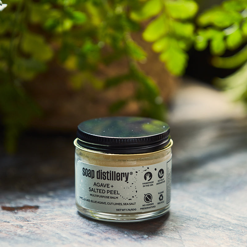 Jar of soap distillery product on a textured surface with greenery in the background