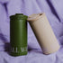 Two matte insulated tumblers resting on draped lavender fabric. One tumbler is olive green with white text reading &