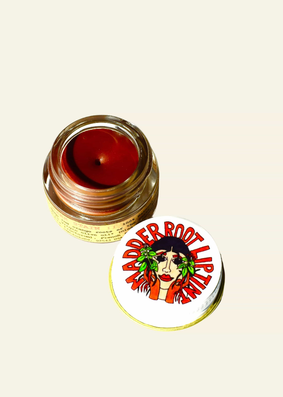 Jar of red lip balm with a label featuring a face and text on a white background