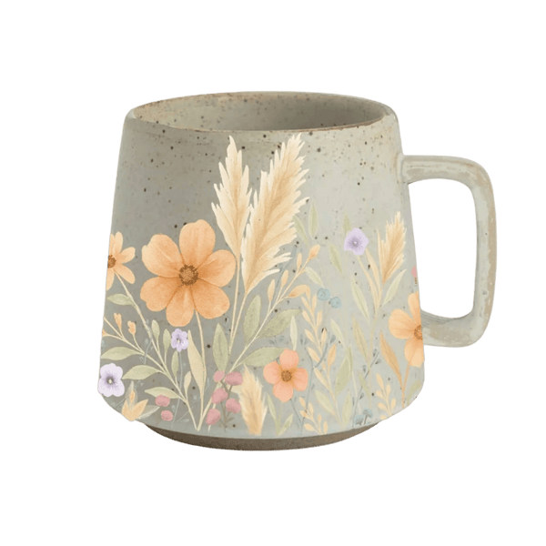 A speckled beige ceramic mug with a floral and botanical illustration on the side, featuring orange flowers, beige grasses, and small purple and pink blossoms, shown on a solid green background.