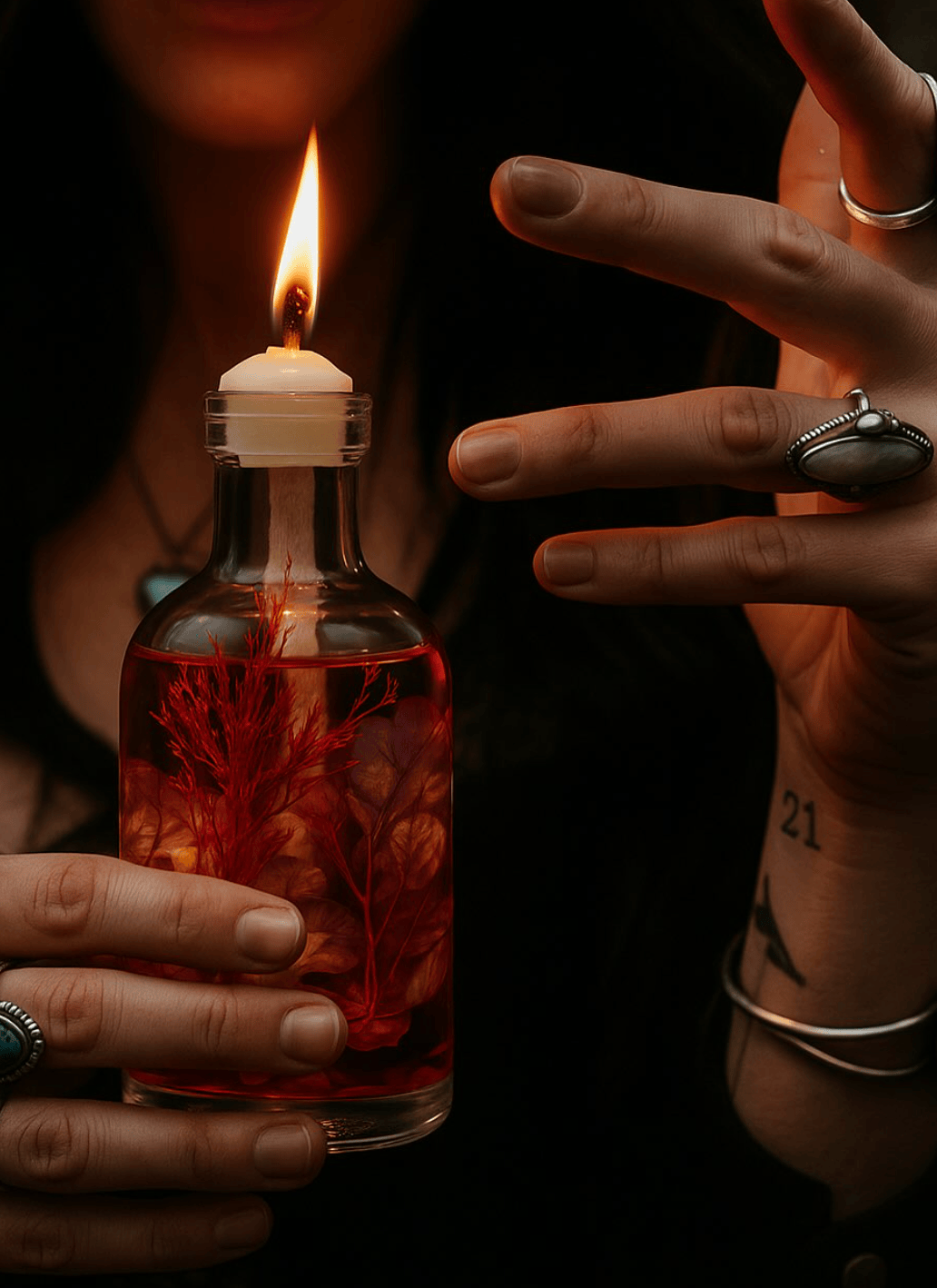 Person holding a lit candle inside a bottle with red liquid and branches.