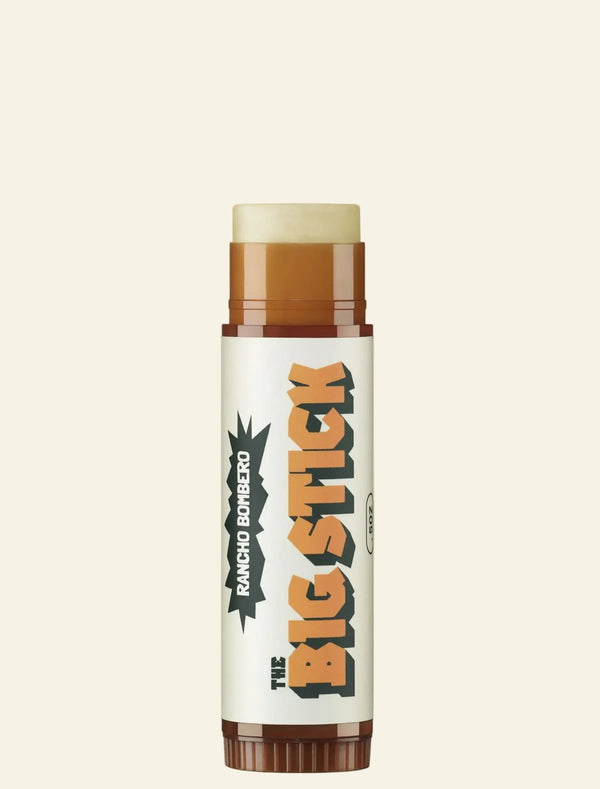 A single stick-style lip balm or cosmetic stick centered on a plain warm beige background. The product has a white label with large orange and black text reading 'THE BIG STICK' and smaller vertical text 'RANCHO BORREGO'.