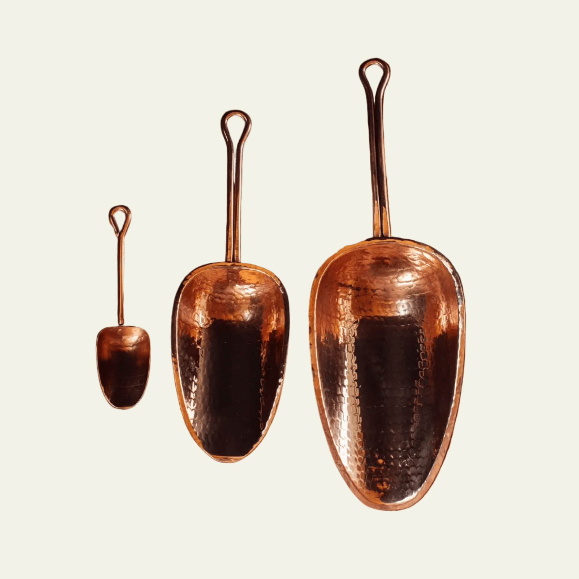 Three copper shovels of varying sizes on a light beige background