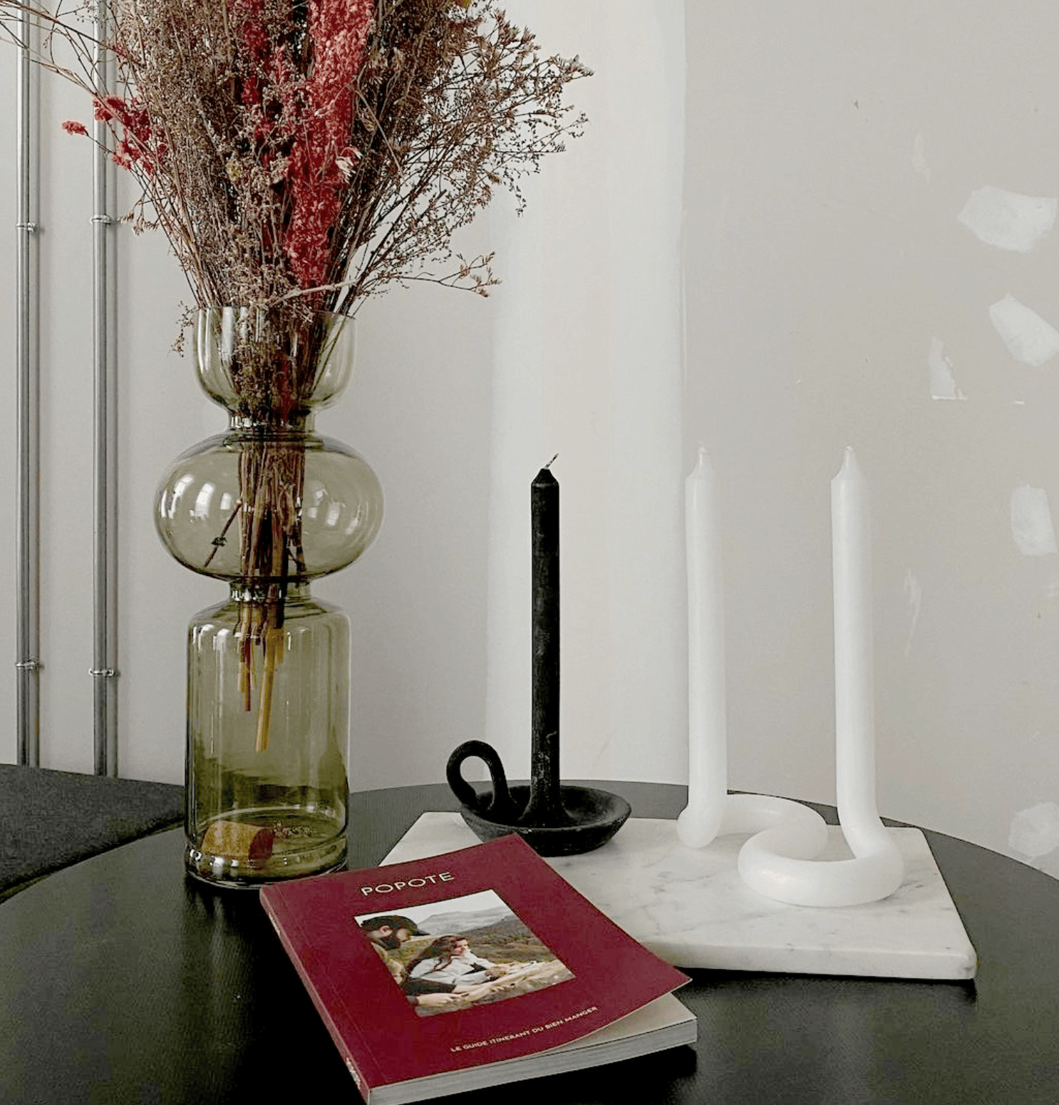 Decorative setup with a vase of dried flowers, candles, and a book on a table.