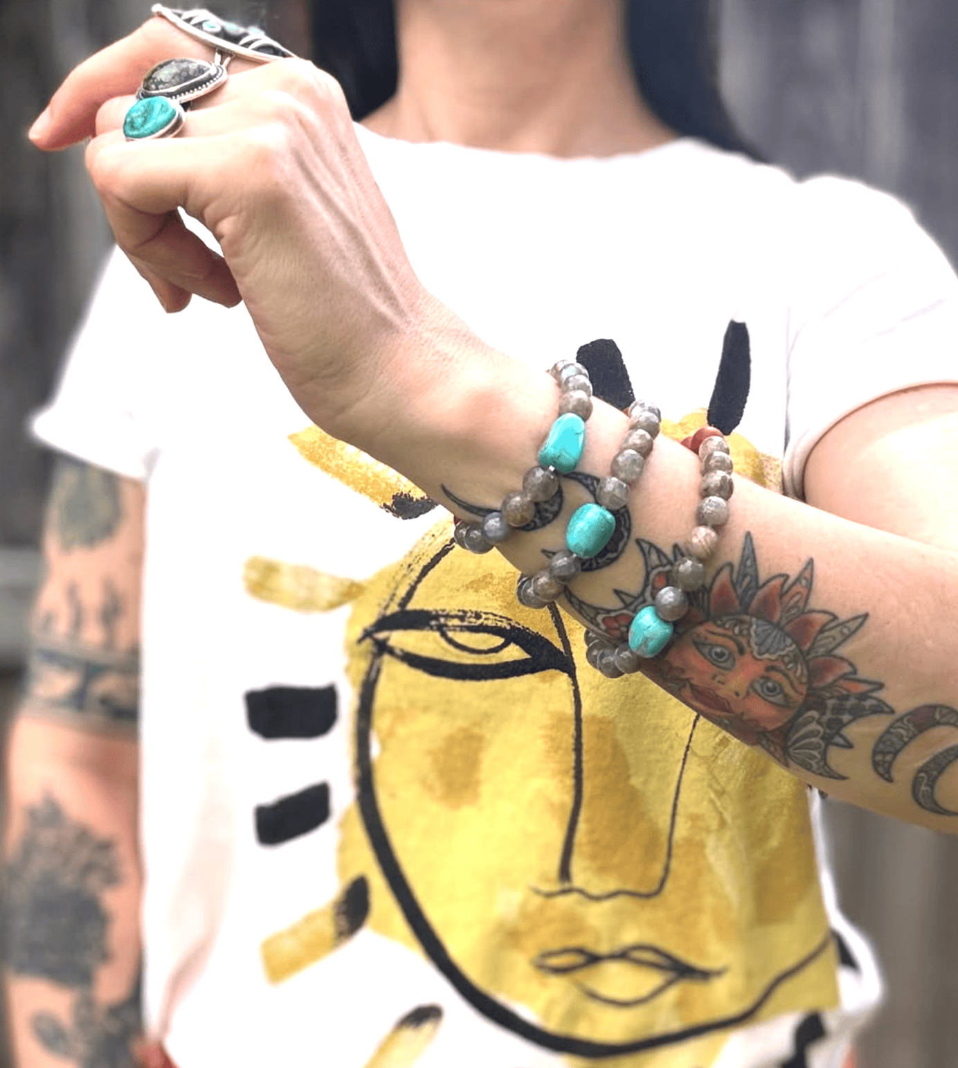 Person wearing bracelets with a tattooed arm in front of a yellow shirt with a face design.