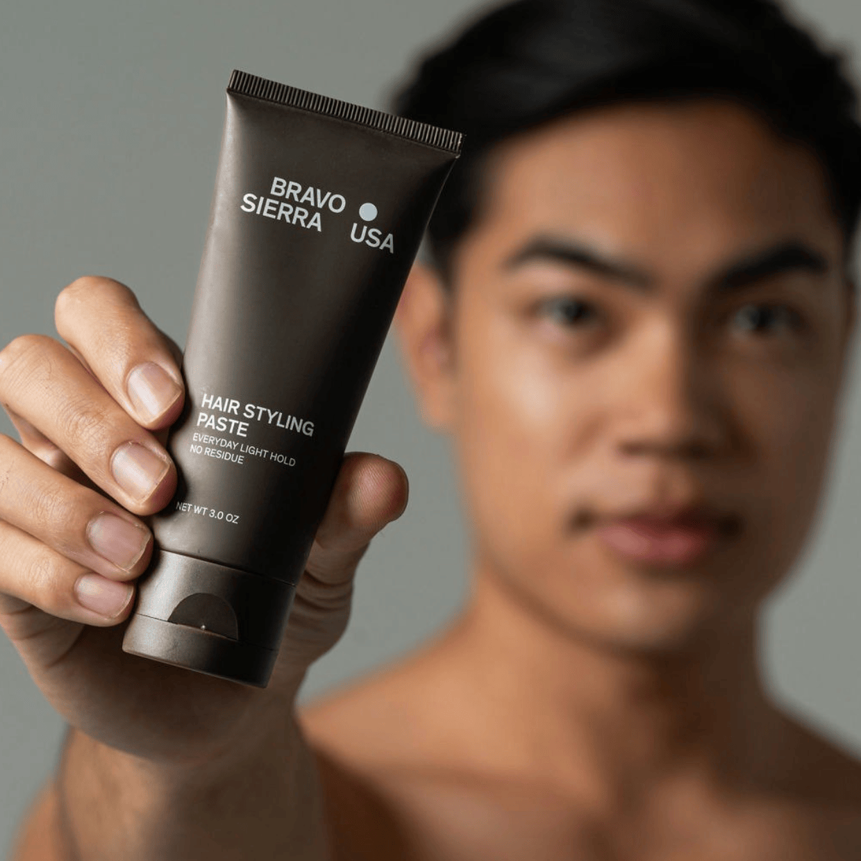 Man holding a tube of Bravo Sierra hair styling paste against a gray background