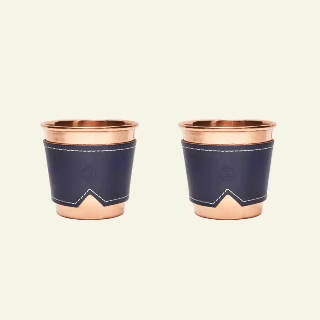 Two copper cups with navy blue leather sleeves on a beige background