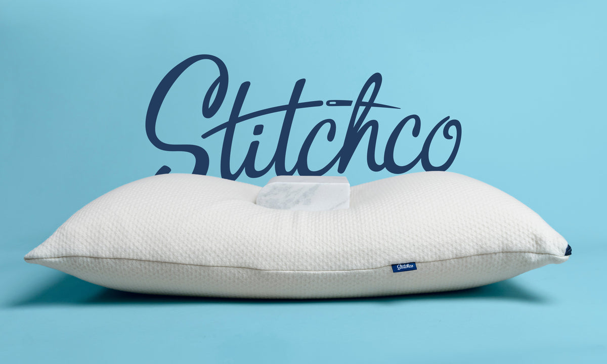A white textured pillow with a central cutout, shown against a light blue background with a large dark blue &