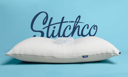 A white textured pillow with a central cutout, shown against a light blue background with a large dark blue &