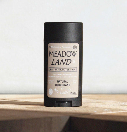 Meadow Land deodorant stick on a wooden surface with a light gray background