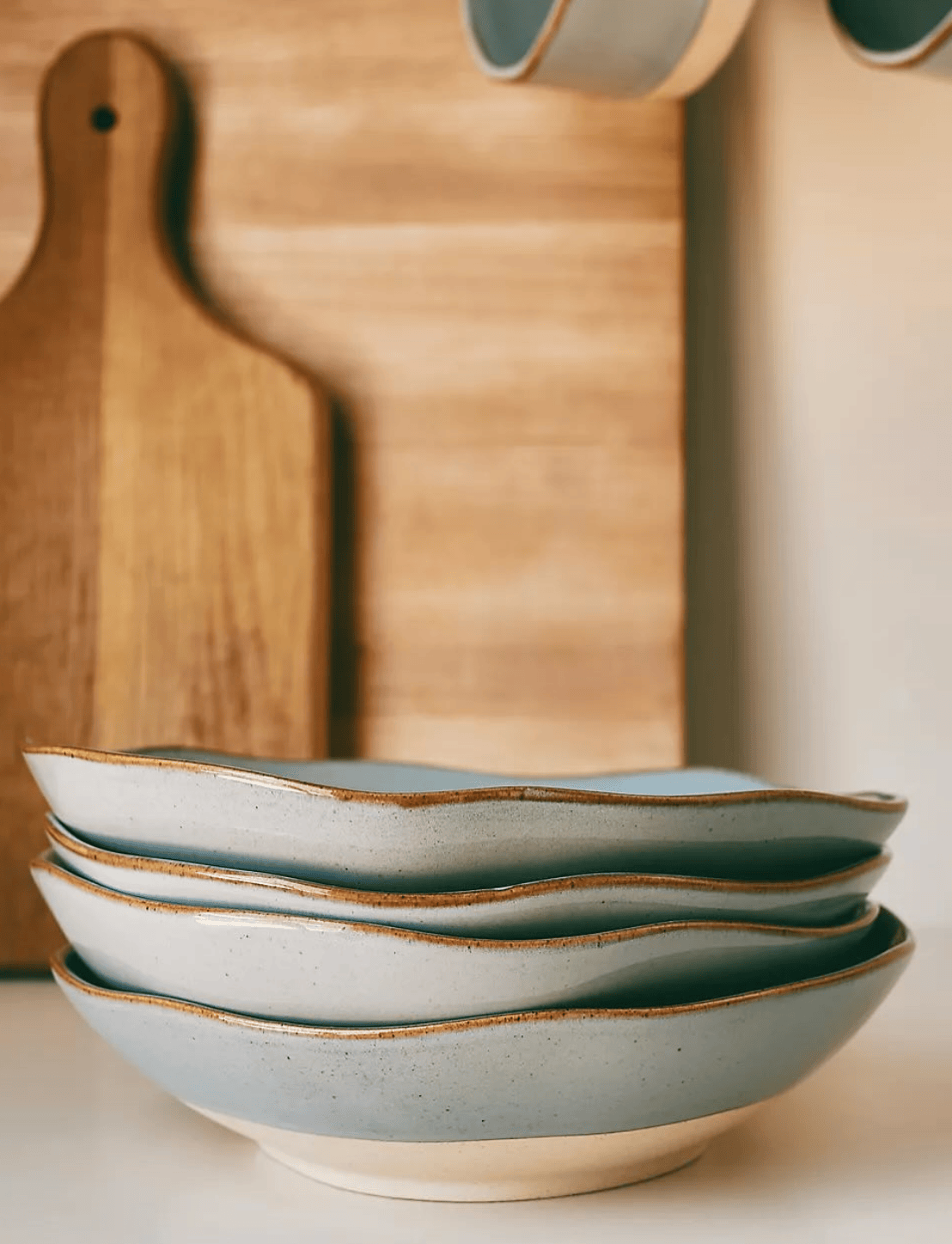 Stack of ceramic bowls with a wooden cutting board in the background