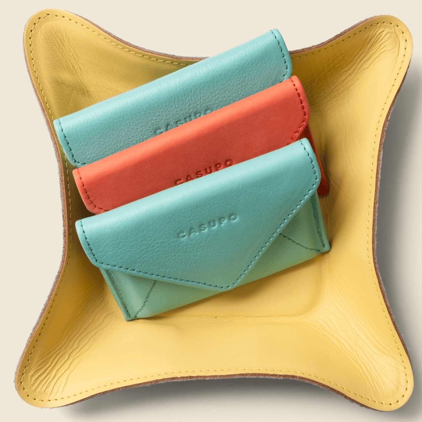 Three small leather wallets in blue and red on a yellow stand with 'CASURO' branding.
