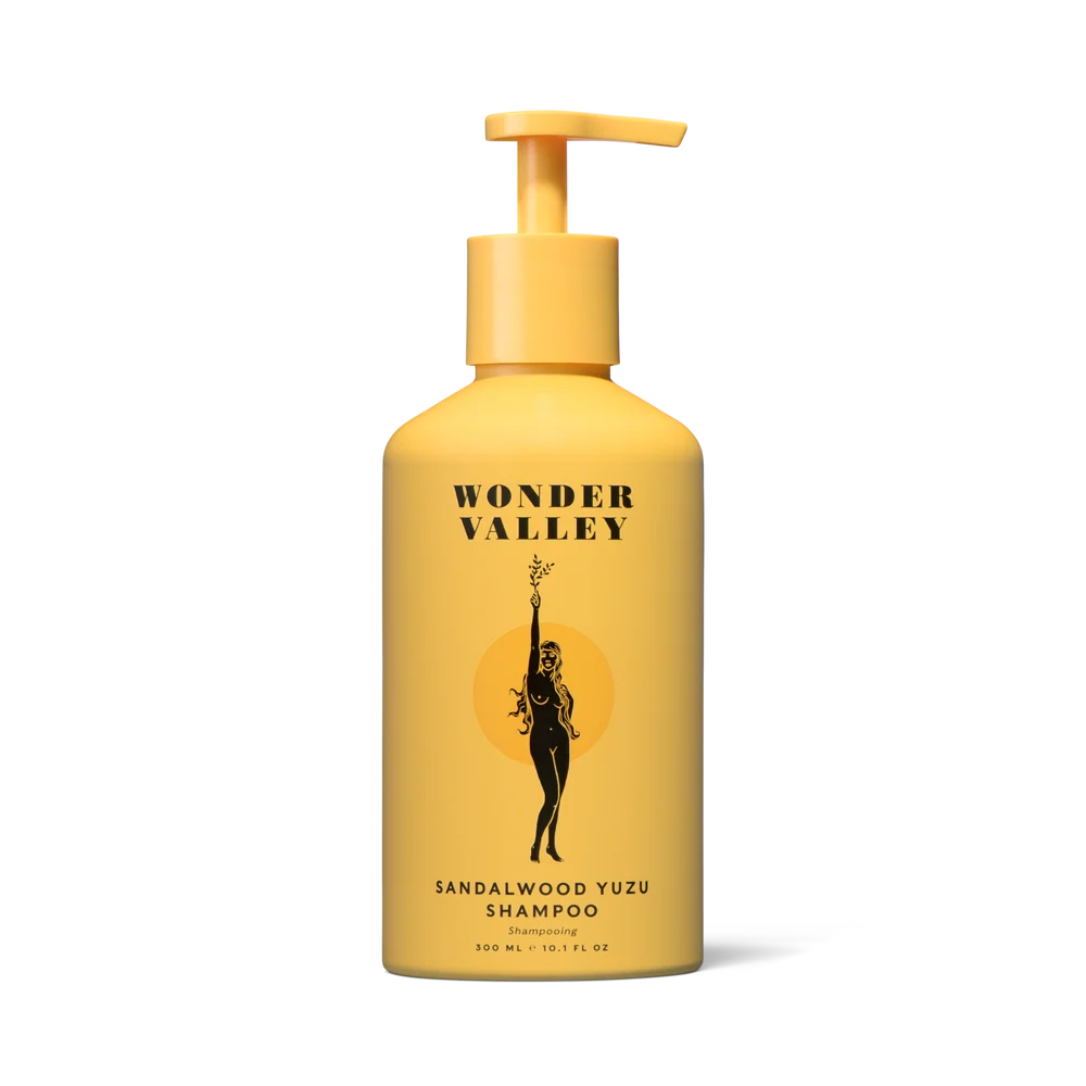 Wonder Valley Sandalwood Yuzu Shampoo in a yellow pump bottle with a black graphic of a woman holding a yuzu and the brand name &