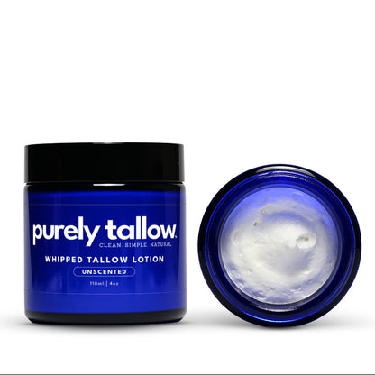 A dark blue jar of Purely Tallow Whipped Tallow Salt Scrub with a black lid, shown next to its open lid revealing white whipped cream inside, on a white background.