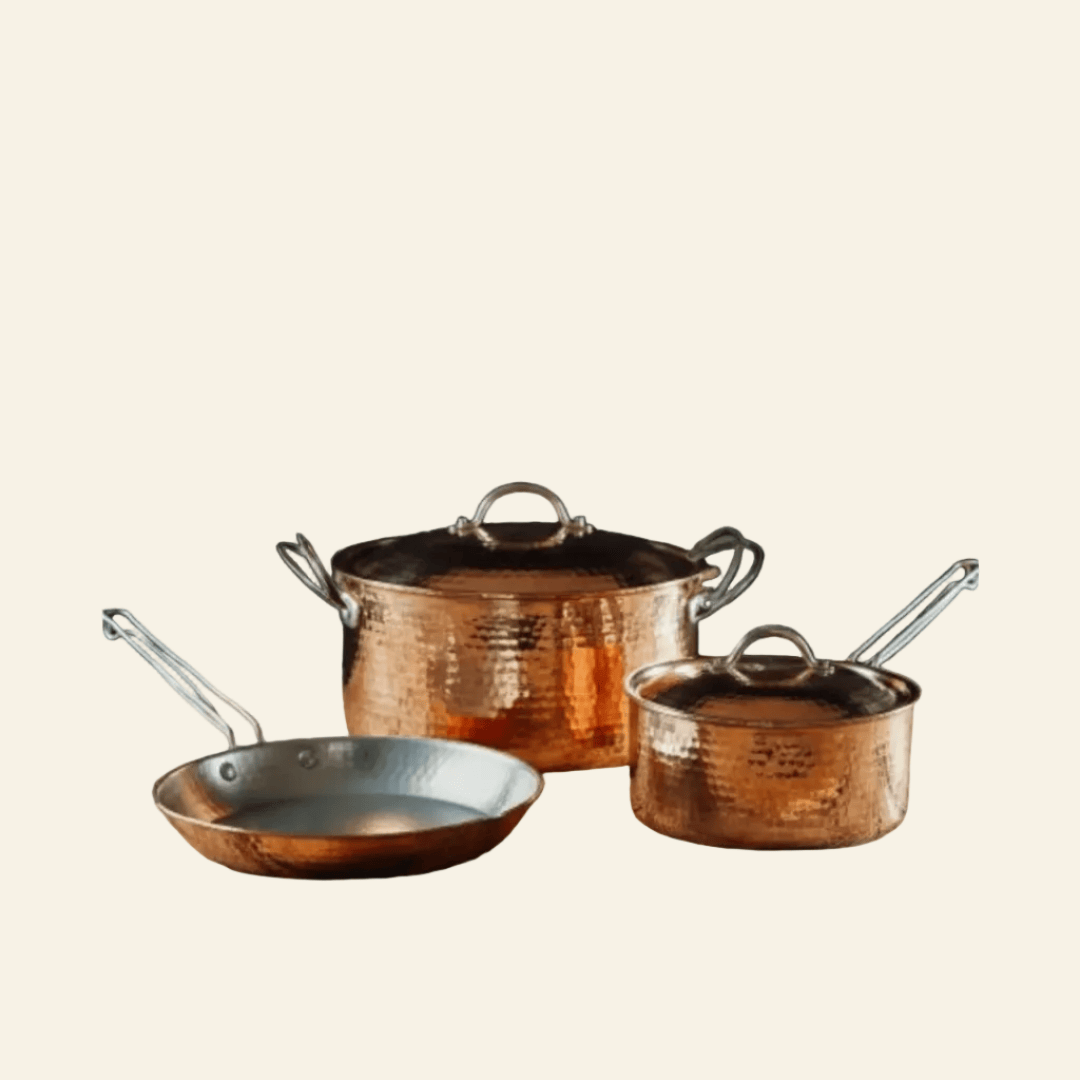 Set of copper cookware including a frying pan, saucepan, and pot on a beige background
