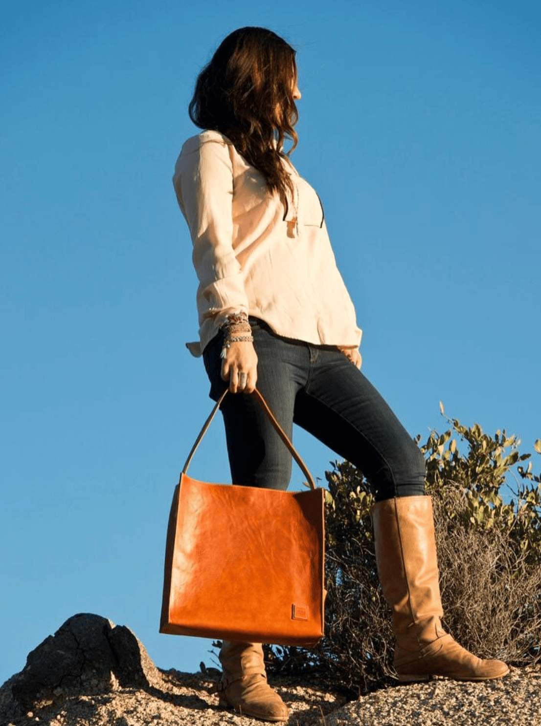 Woman holding a brown leather bag against a clear blue sky