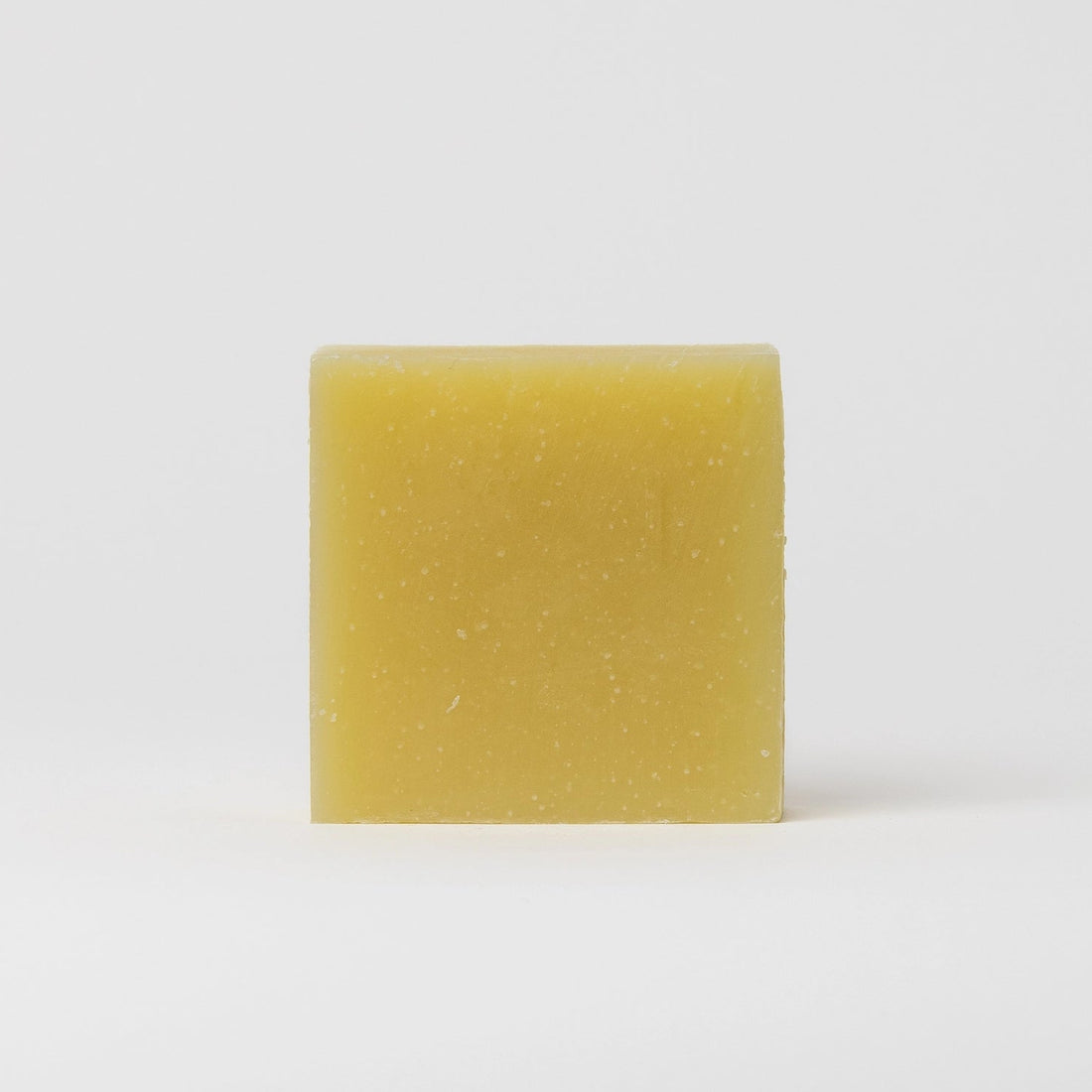 A single rectangular bar of pale yellow soap with small white specks, standing upright against a clean white background.