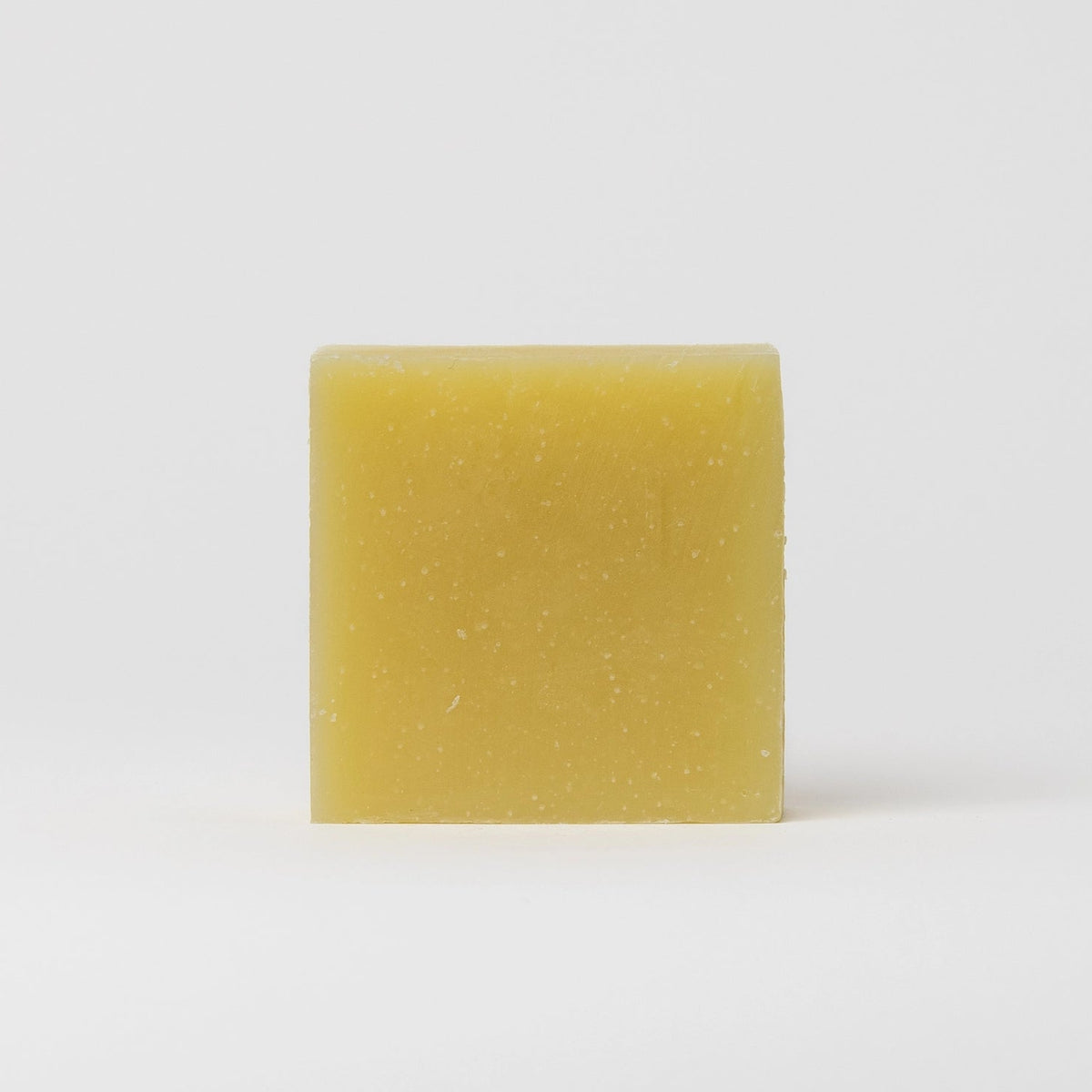 A single rectangular bar of pale yellow soap with small white specks, standing upright against a clean white background.
