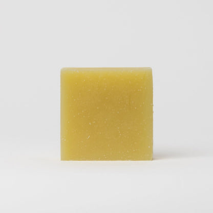A single rectangular bar of pale yellow soap with small white specks, standing upright against a clean white background.