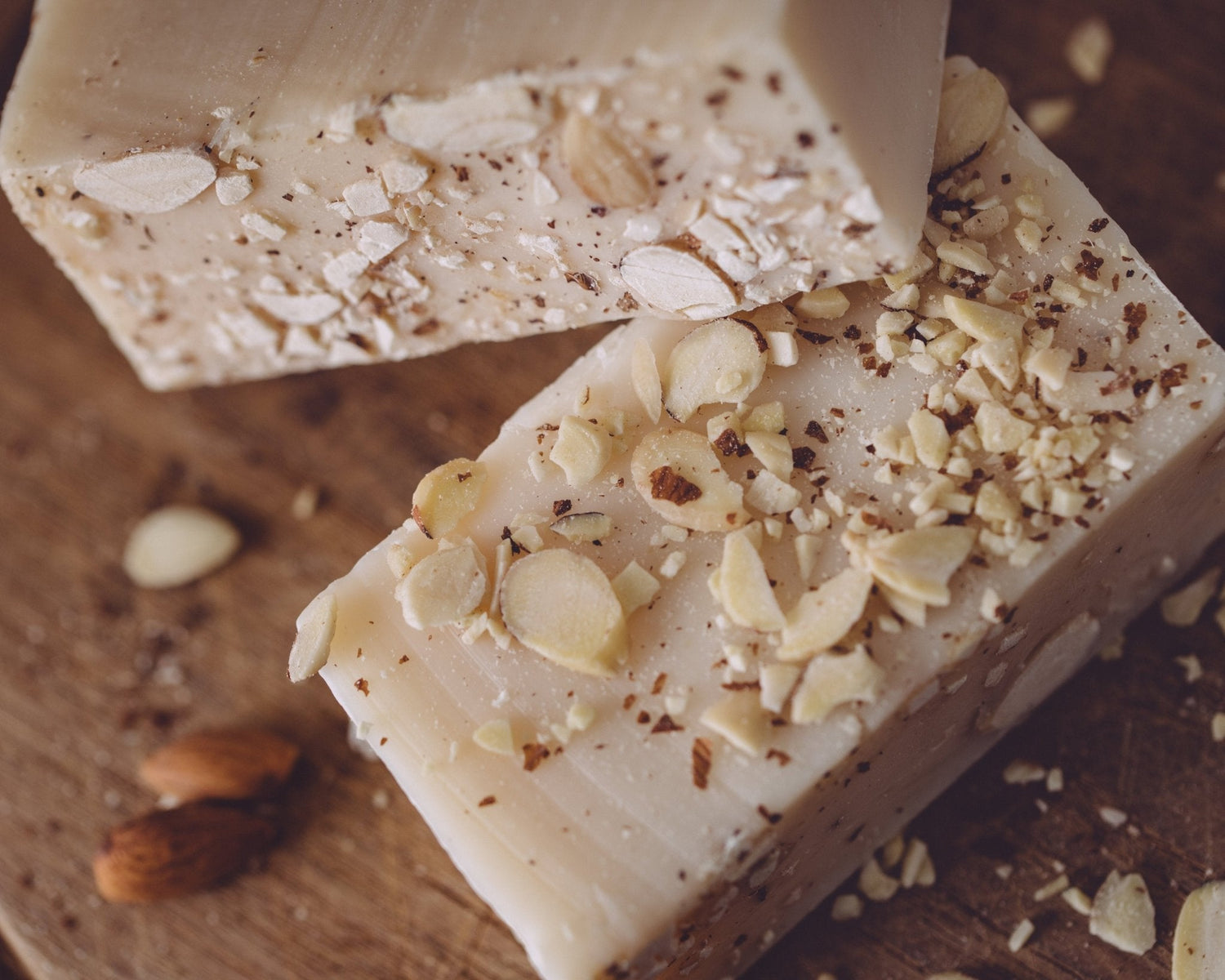 Two bars of soap with almond pieces on a wooden surface