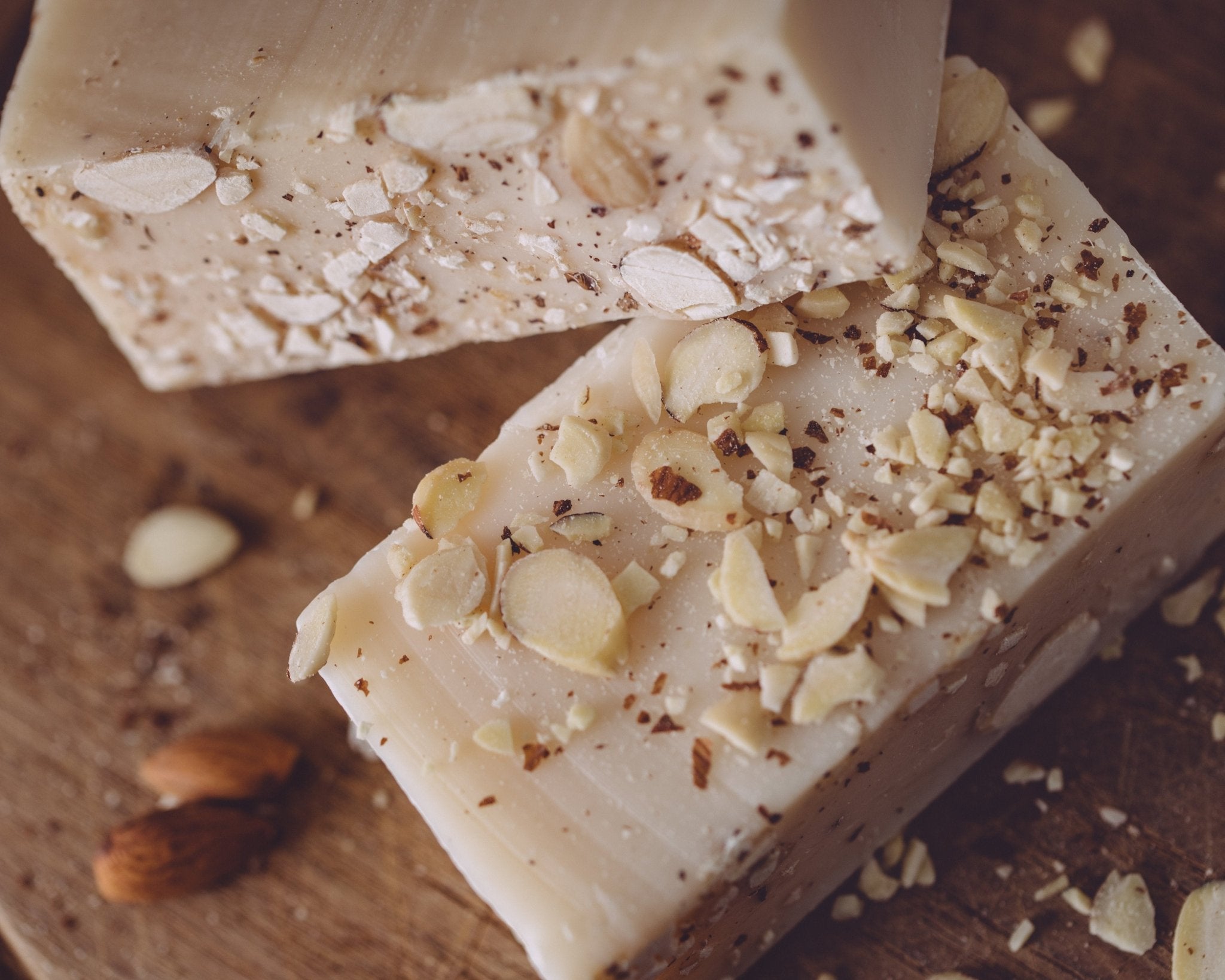 Two bars of soap with almond pieces on a wooden surface