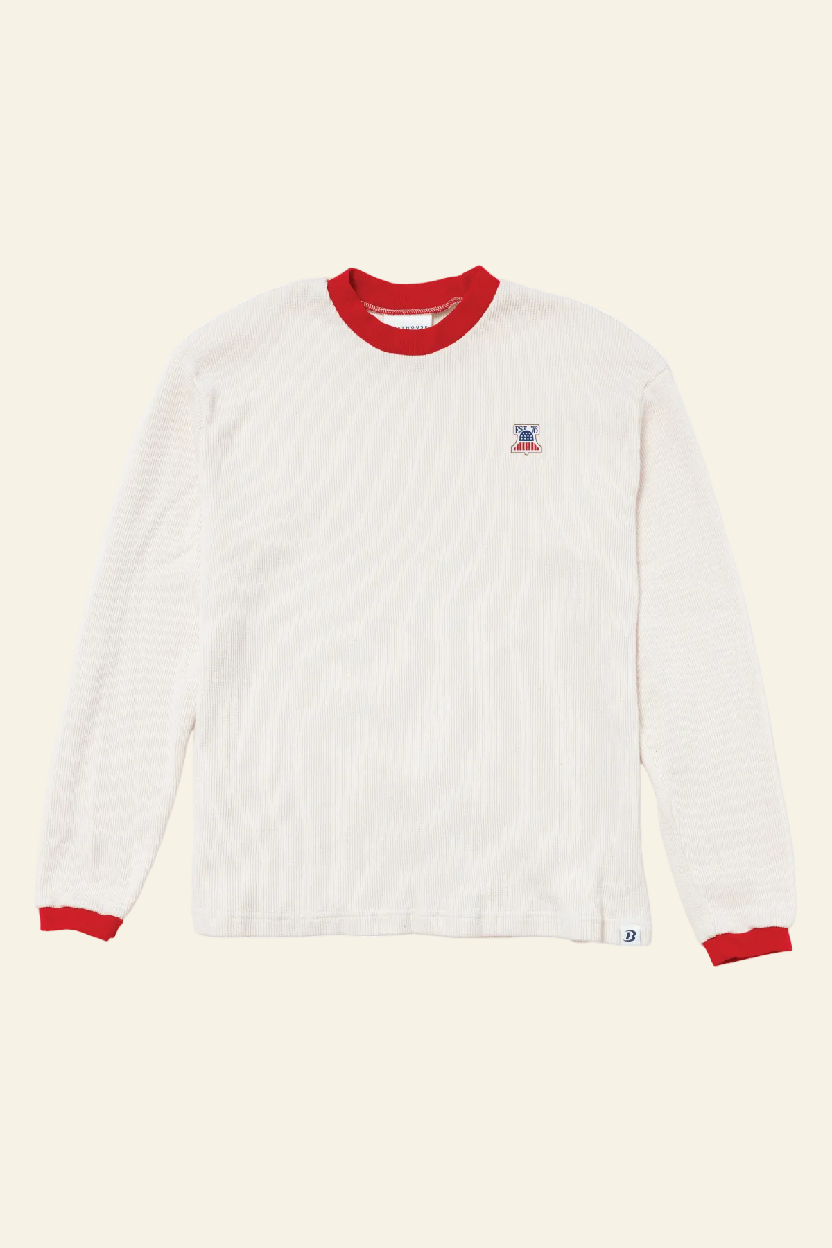 An off-white long-sleeve t-shirt with red ribbed collar and cuffs, featuring a small embroidered logo on the left chest and a small white tag near the bottom hem, displayed on a clean white background.