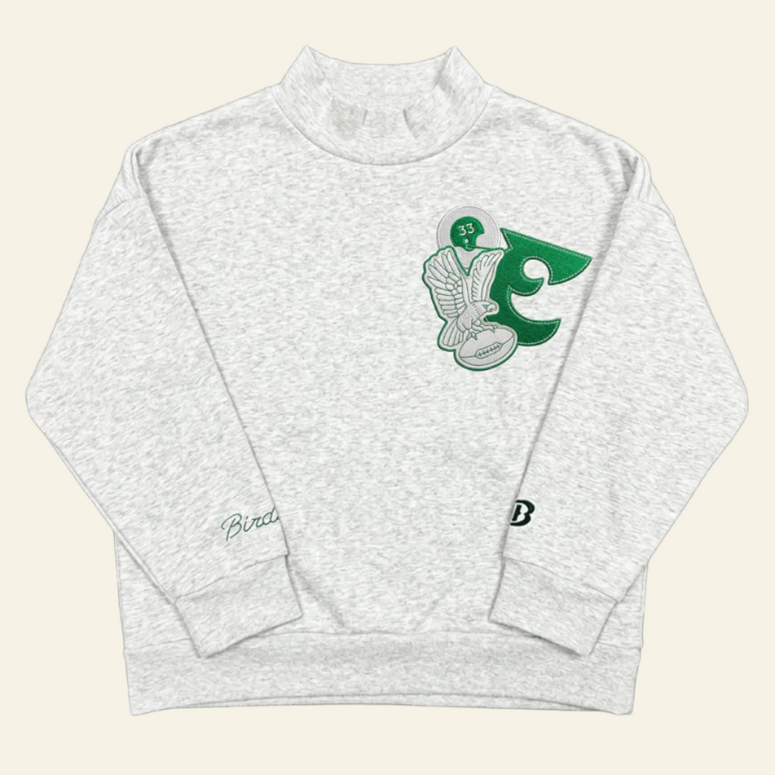 A light heather gray long-sleeve mock neck sweatshirt featuring a green and white graphic of a hockey player and the number 5 on the left chest, with a small script logo on the right sleeve and a small &