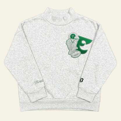 A light heather gray long-sleeve mock neck sweatshirt featuring a green and white graphic of a hockey player and the number 5 on the left chest, with a small script logo on the right sleeve and a small &