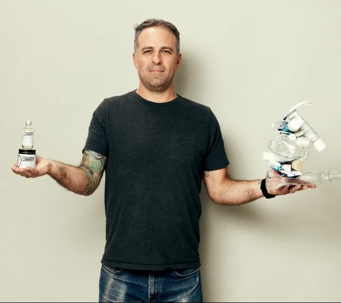 Man holding two small robots against a plain background