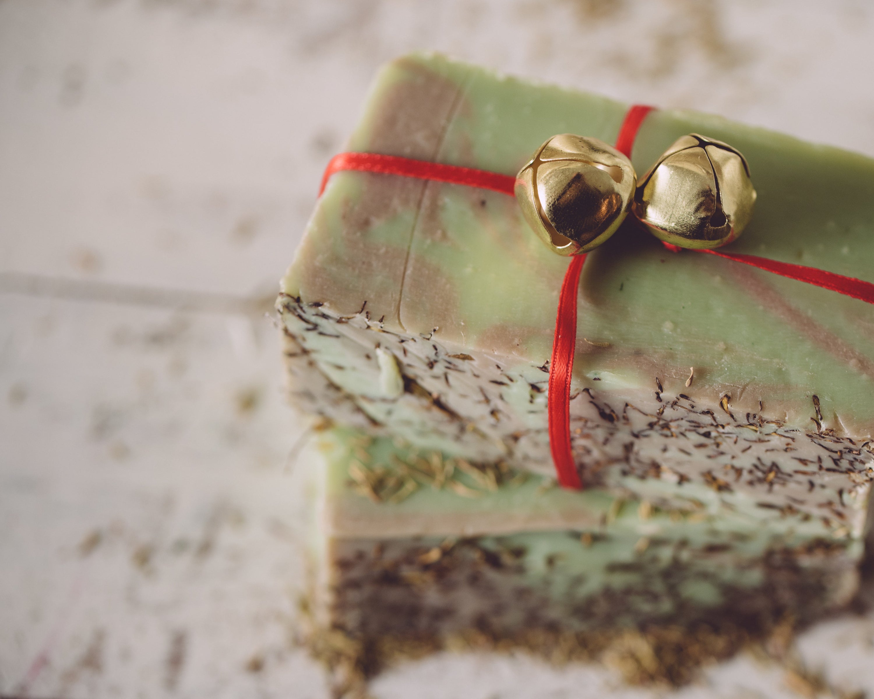Green soap bar with gold bells and red string on a textured surface